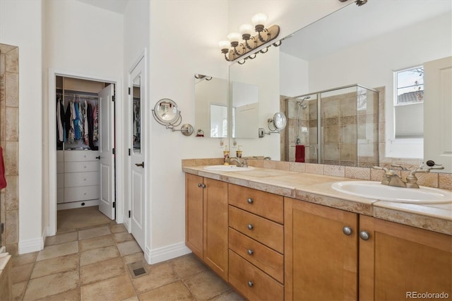 full bath with double vanity, a shower stall, a walk in closet, and a sink