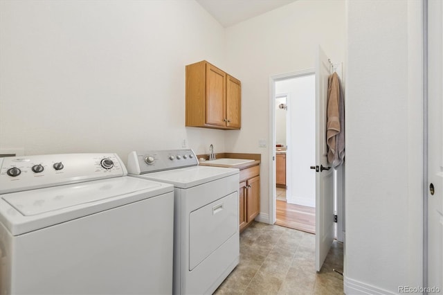 clothes washing area with washer and dryer, baseboards, cabinet space, and a sink