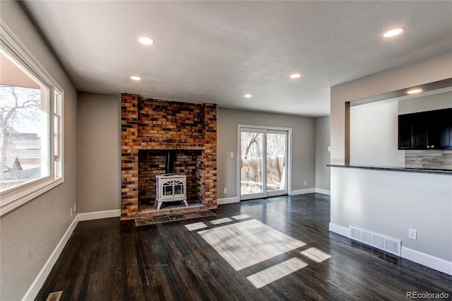 unfurnished living room featuring dark wood-type flooring, a wood stove, and a textured ceiling