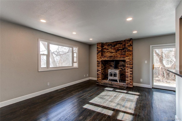 unfurnished living room featuring a textured ceiling, dark wood-type flooring, and a wood stove