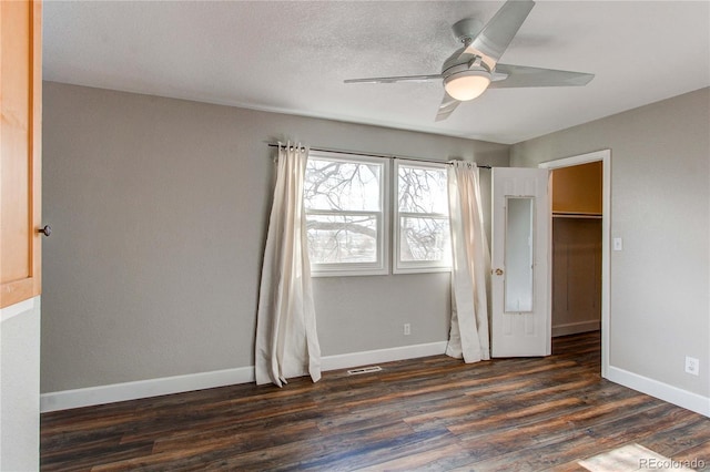 unfurnished bedroom with dark wood-type flooring, ceiling fan, a walk in closet, and a closet