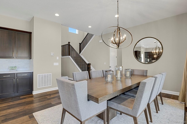 dining area with dark wood-style flooring, visible vents, an inviting chandelier, baseboards, and stairs