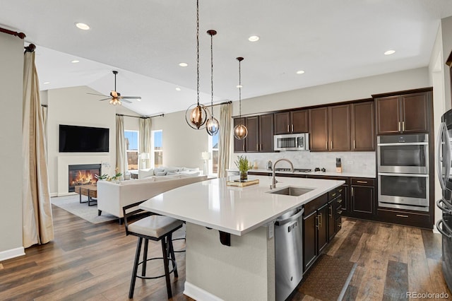 kitchen with appliances with stainless steel finishes, dark wood finished floors, a sink, and a glass covered fireplace