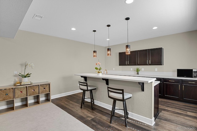 kitchen featuring dark wood-style floors, a kitchen bar, light countertops, stainless steel microwave, and baseboards