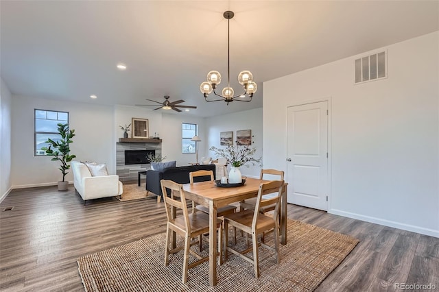 dining area with a fireplace, dark wood finished floors, ceiling fan with notable chandelier, baseboards, and visible vents