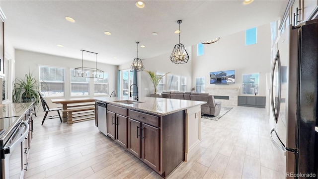 kitchen with a kitchen island with sink, stainless steel appliances, a sink, light stone countertops, and pendant lighting