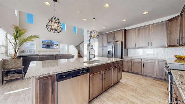 kitchen with appliances with stainless steel finishes, an island with sink, a sink, and light stone counters