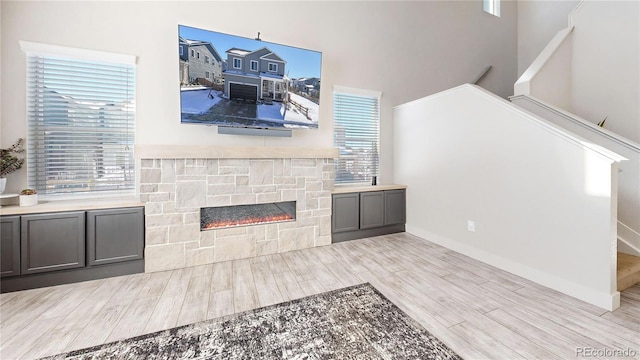 living area with stairs, a fireplace, light wood-style flooring, and baseboards