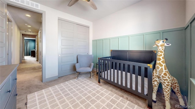 bedroom with light carpet, a nursery area, visible vents, and a decorative wall