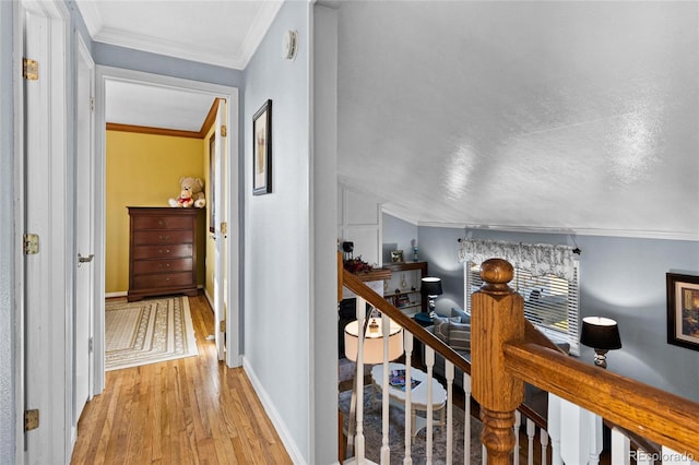 hallway with light hardwood / wood-style flooring, ornamental molding, a textured ceiling, and vaulted ceiling