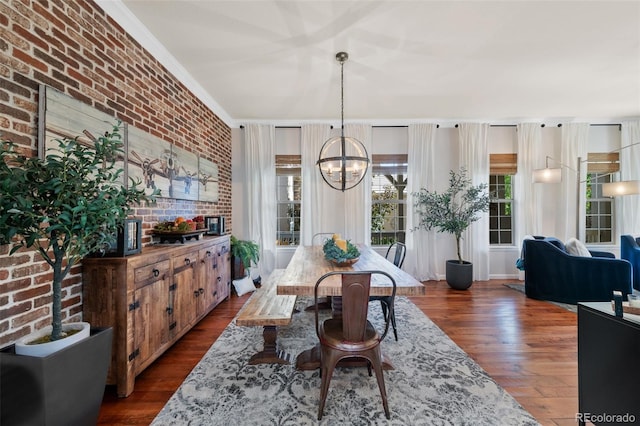 dining space with dark wood-type flooring, brick wall, ornamental molding, and a chandelier