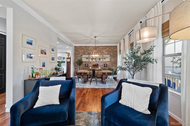 interior space with a notable chandelier, brick wall, wood-type flooring, and ornamental molding