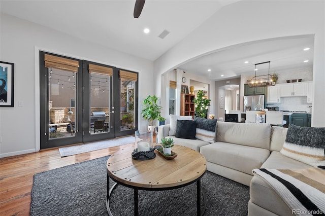 living room featuring lofted ceiling, ceiling fan with notable chandelier, and light hardwood / wood-style floors