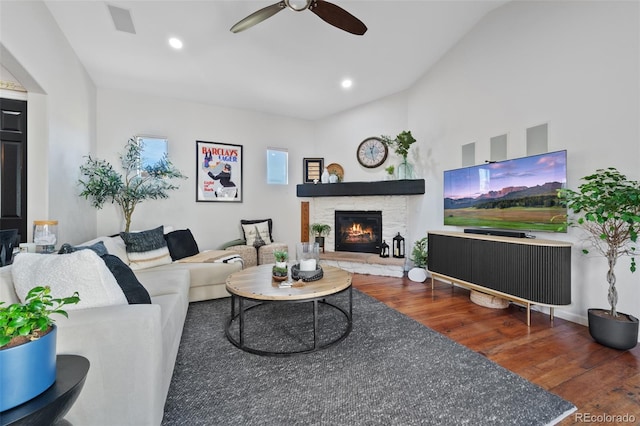 living room with a stone fireplace, ceiling fan, vaulted ceiling, and dark hardwood / wood-style flooring