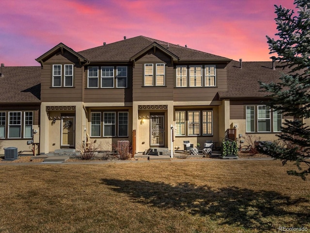 view of front of home featuring a yard, roof with shingles, central AC unit, and stucco siding