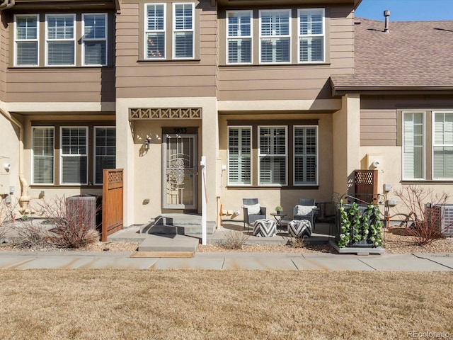 entrance to property featuring stucco siding, central AC, and a shingled roof