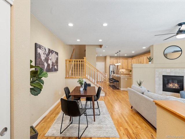 dining area with baseboards, recessed lighting, a tile fireplace, stairs, and light wood-type flooring