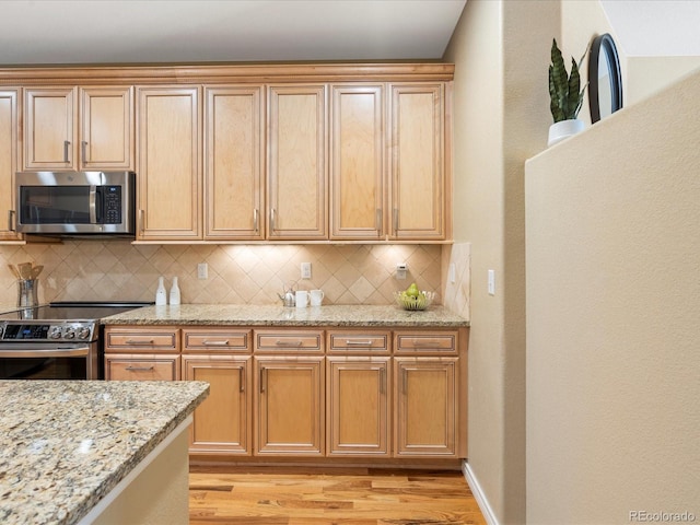 kitchen featuring light stone counters, baseboards, light wood-style floors, appliances with stainless steel finishes, and backsplash