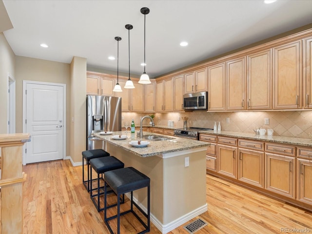 kitchen featuring visible vents, a breakfast bar, a sink, stainless steel appliances, and light wood finished floors