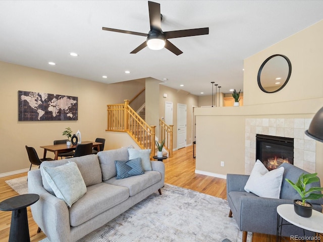 living area with baseboards, a tiled fireplace, stairs, recessed lighting, and light wood-style flooring