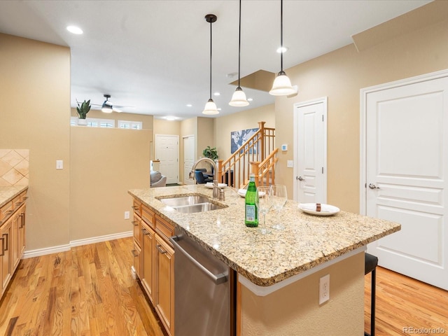 kitchen with a sink, light wood-style floors, stainless steel dishwasher, and a breakfast bar