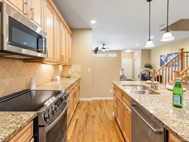 kitchen featuring tasteful backsplash, light wood-type flooring, stainless steel appliances, a ceiling fan, and a sink