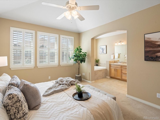 bedroom featuring light carpet, a ceiling fan, ensuite bath, arched walkways, and baseboards