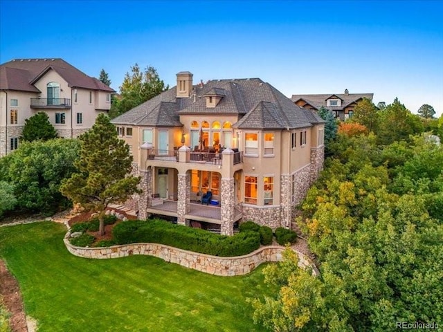 back of property featuring stone siding, a lawn, and a balcony