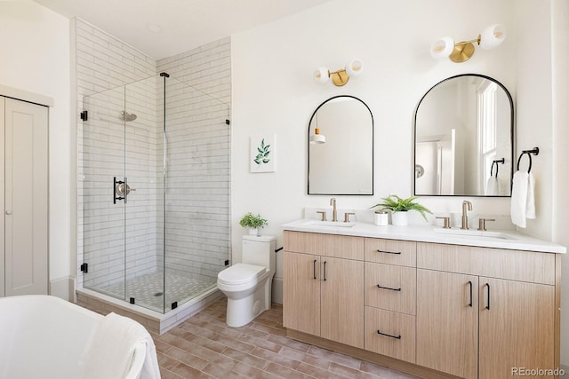 bathroom featuring double vanity, a shower stall, toilet, and a sink