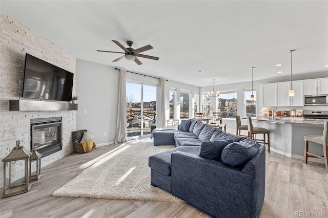 living room featuring ceiling fan with notable chandelier, light hardwood / wood-style floors, a textured ceiling, and a fireplace