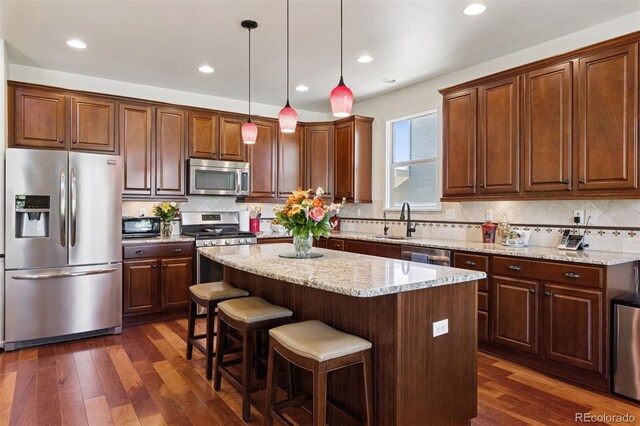 12189 Windy Trail Ln, Parker, CO 80138 - kitchen with stainless steel appliances, a sink, dark wood finished floors, a center island, and tasteful backsplash