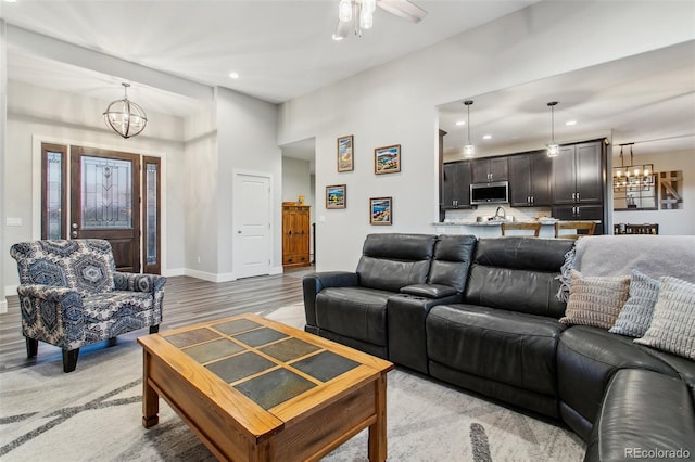 living area with recessed lighting, ceiling fan with notable chandelier, baseboards, and light wood finished floors