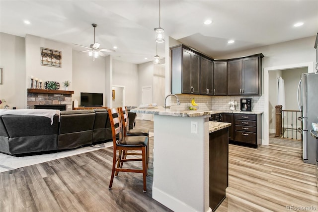 kitchen featuring dark brown cabinets, a kitchen bar, light stone counters, a peninsula, and freestanding refrigerator