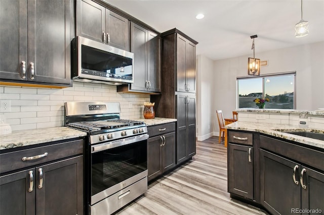 kitchen with stainless steel appliances, light wood-style floors, pendant lighting, and decorative backsplash