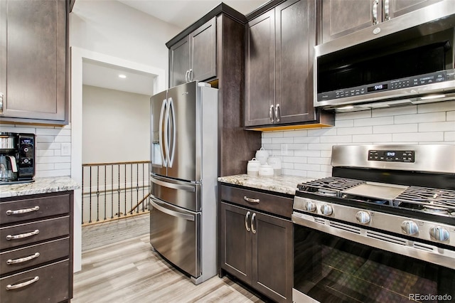 kitchen featuring light stone counters, light wood-style flooring, stainless steel appliances, decorative backsplash, and dark brown cabinets