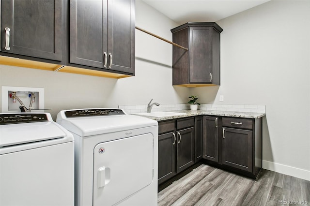 washroom featuring washing machine and clothes dryer, baseboards, light wood-style flooring, cabinet space, and a sink