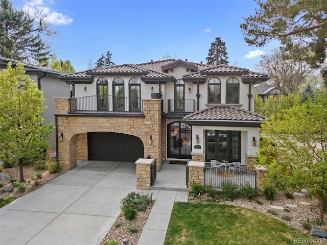 mediterranean / spanish-style house with a garage, stucco siding, a balcony, french doors, and driveway