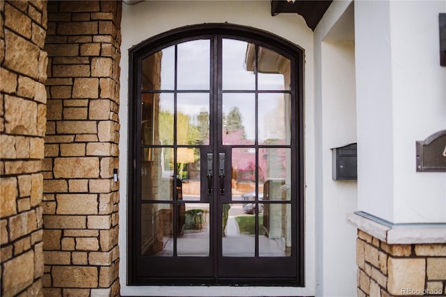 doorway to property with stucco siding, french doors, and stone siding