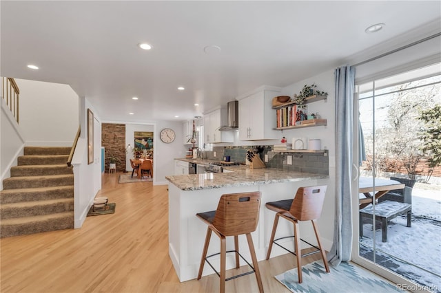 kitchen with open shelves, white cabinets, wall chimney exhaust hood, and light wood-style floors