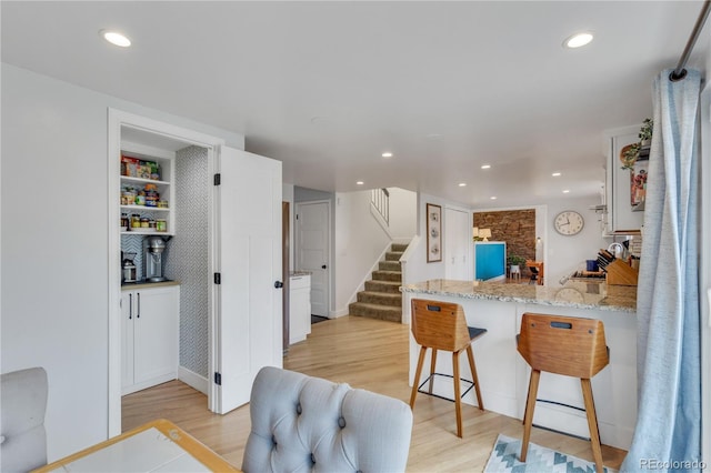 kitchen with light wood finished floors, a kitchen bar, light stone counters, recessed lighting, and a peninsula