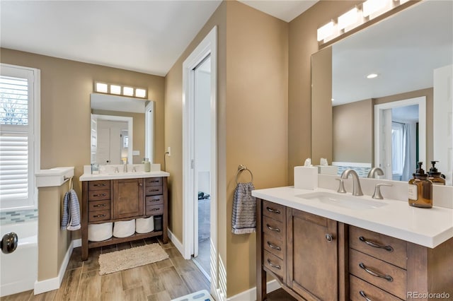 bathroom with two vanities, wood finished floors, baseboards, and a sink