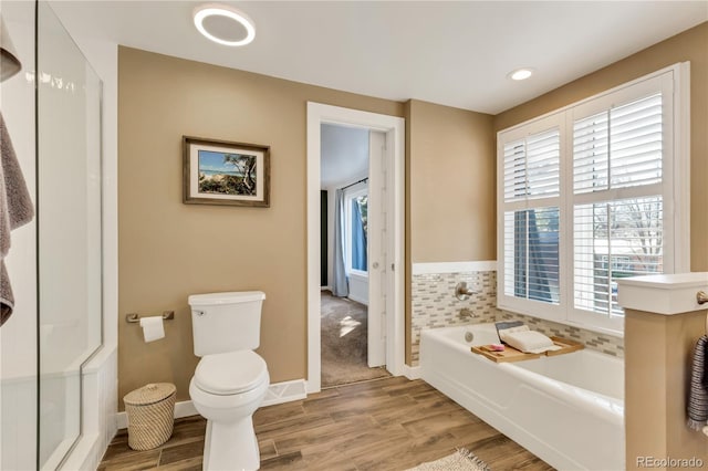 full bathroom featuring baseboards, wood finished floors, toilet, and a bath