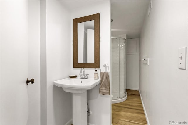 bathroom featuring a sink, baseboards, wood finished floors, and a shower stall