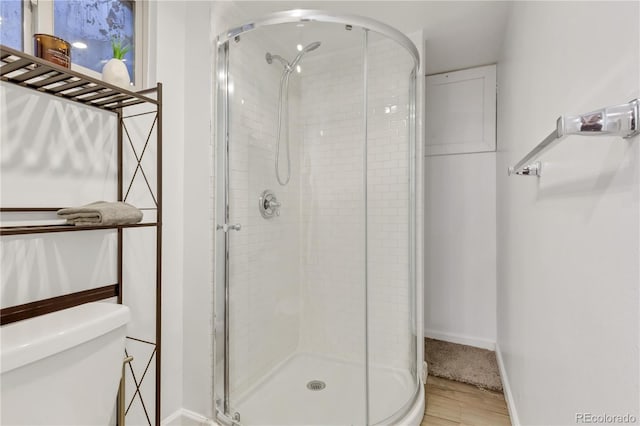 bathroom with baseboards, toilet, wood finished floors, and a shower stall