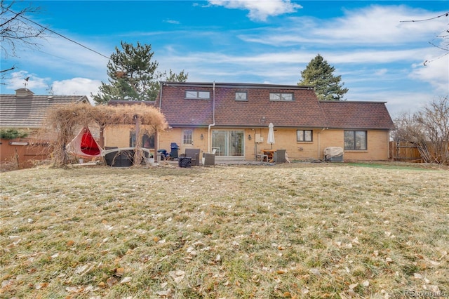 rear view of property with brick siding, a lawn, and fence