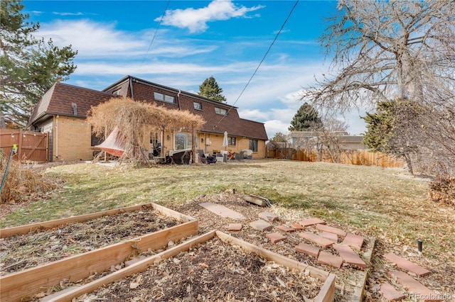 rear view of house featuring brick siding, a lawn, mansard roof, a fenced backyard, and a garden