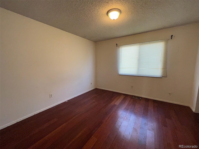 empty room with dark hardwood / wood-style flooring and a textured ceiling