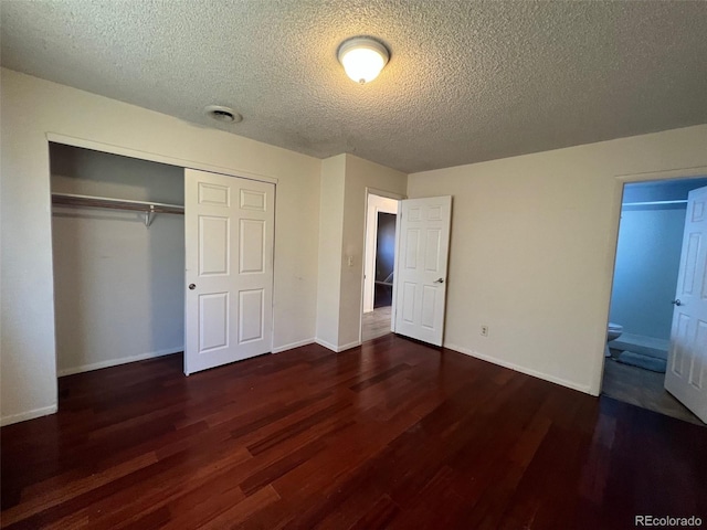 unfurnished bedroom with a closet, dark wood-type flooring, connected bathroom, and a textured ceiling