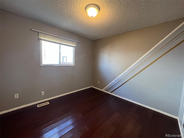 spare room with a textured ceiling and dark hardwood / wood-style floors