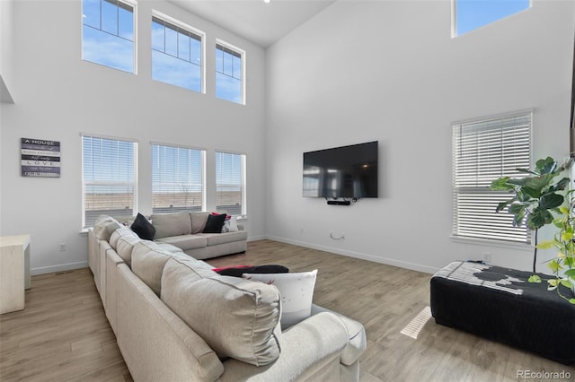 living area featuring light wood-style flooring, a high ceiling, and baseboards